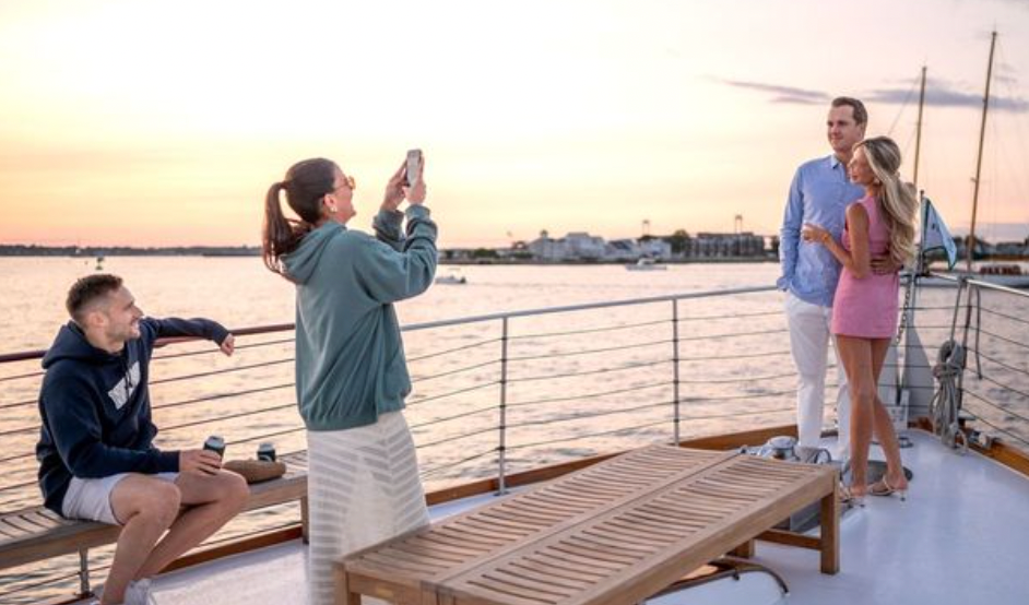 Friends on a boat at sunset; two posing, one taking a photo.
