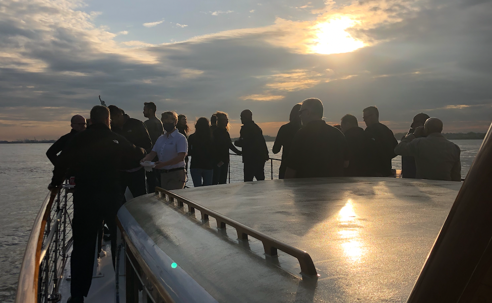 Group of people on a boat at sunset under a partly cloudy sky.