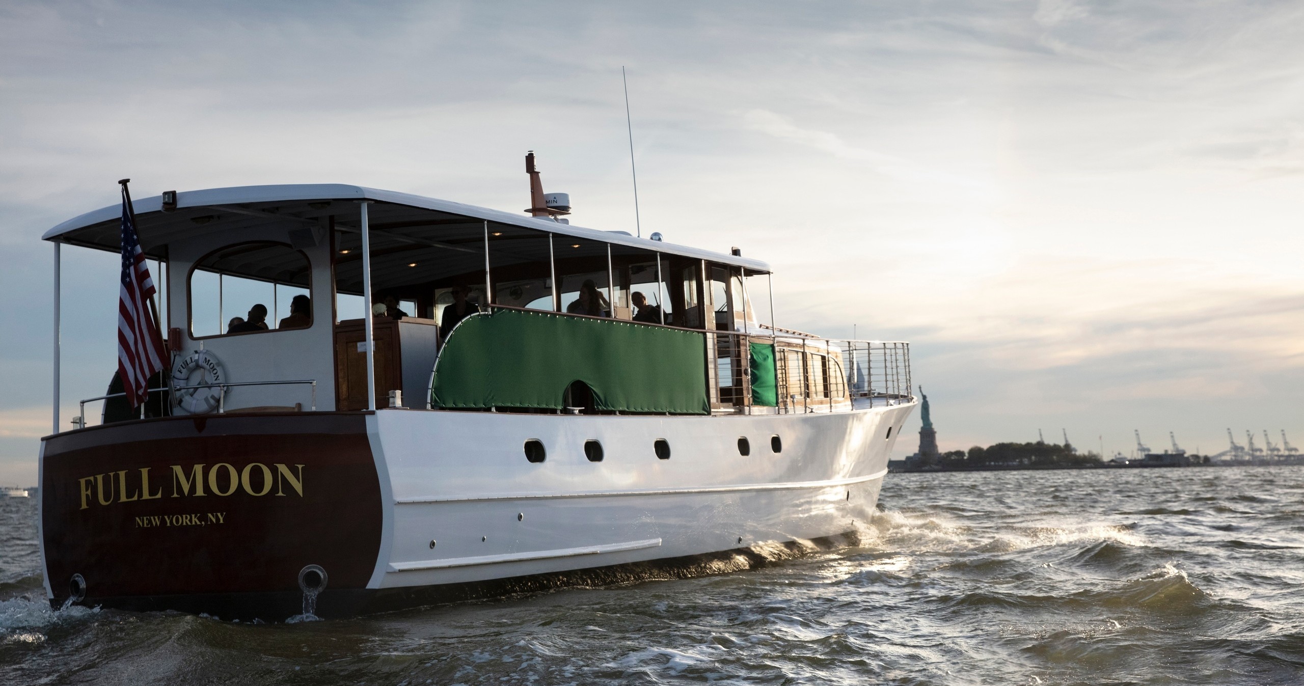 Boat named 'Full Moon' on water with Statue of Liberty in background.