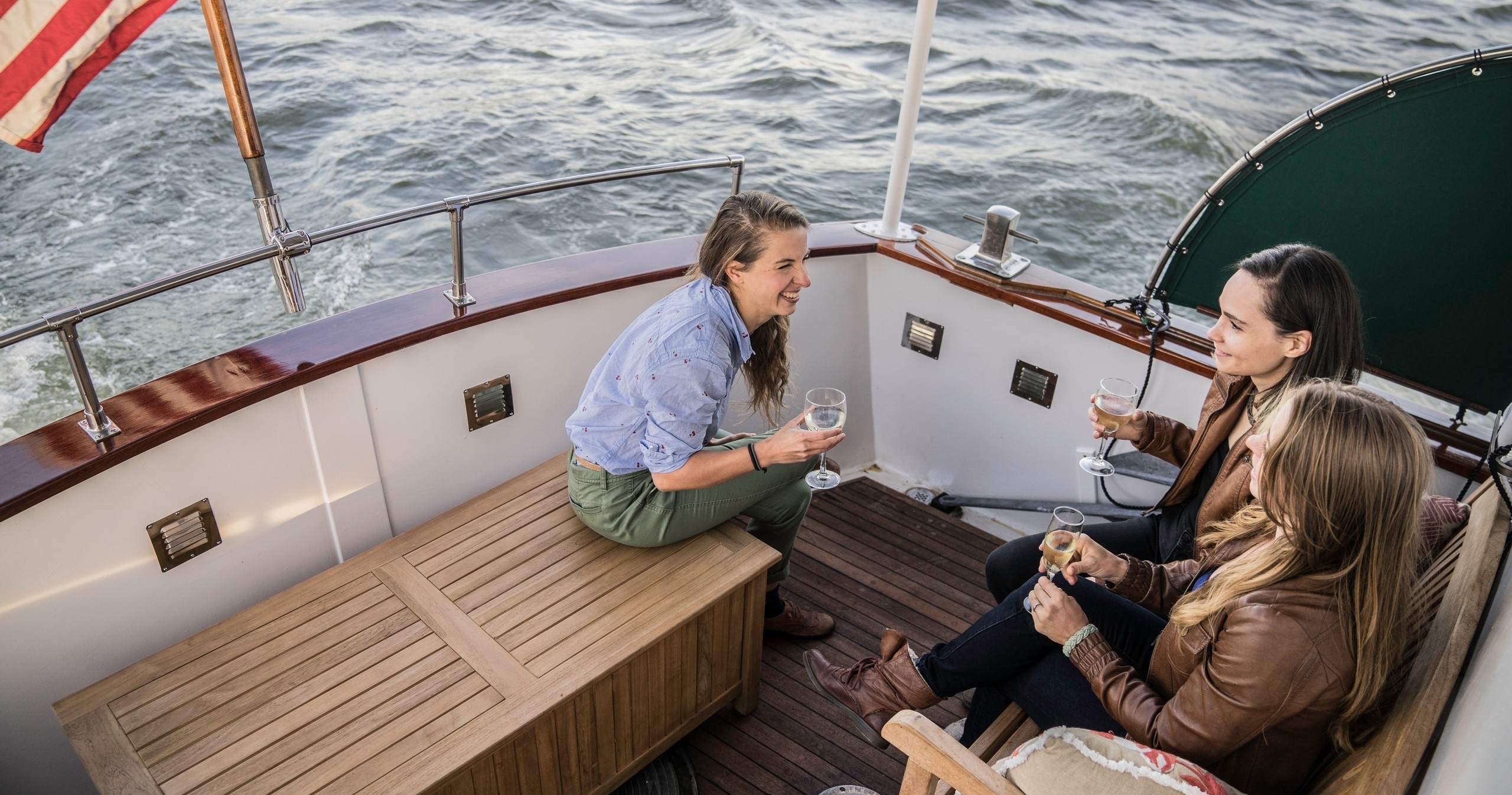 Three people chat and drink on a boat with waves in the background.