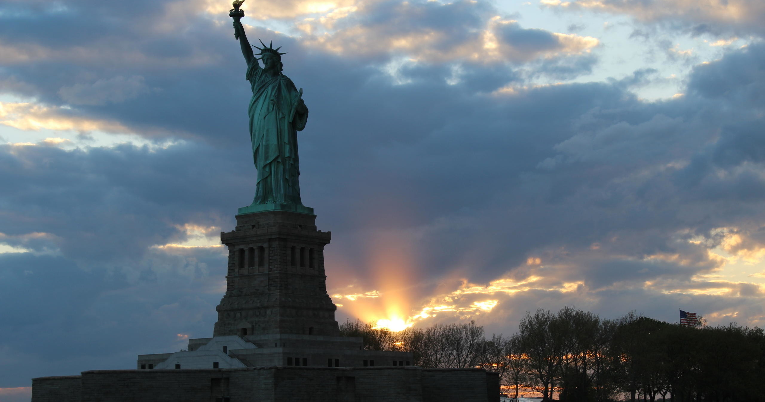 Statue of Liberty silhouetted against a sunrise with clouds and sun rays.