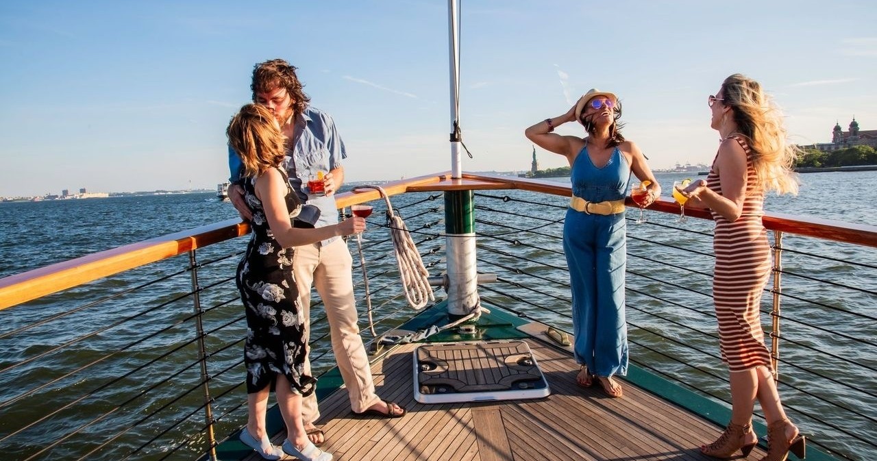 Four people enjoying drinks on a boat deck with a scenic water view.