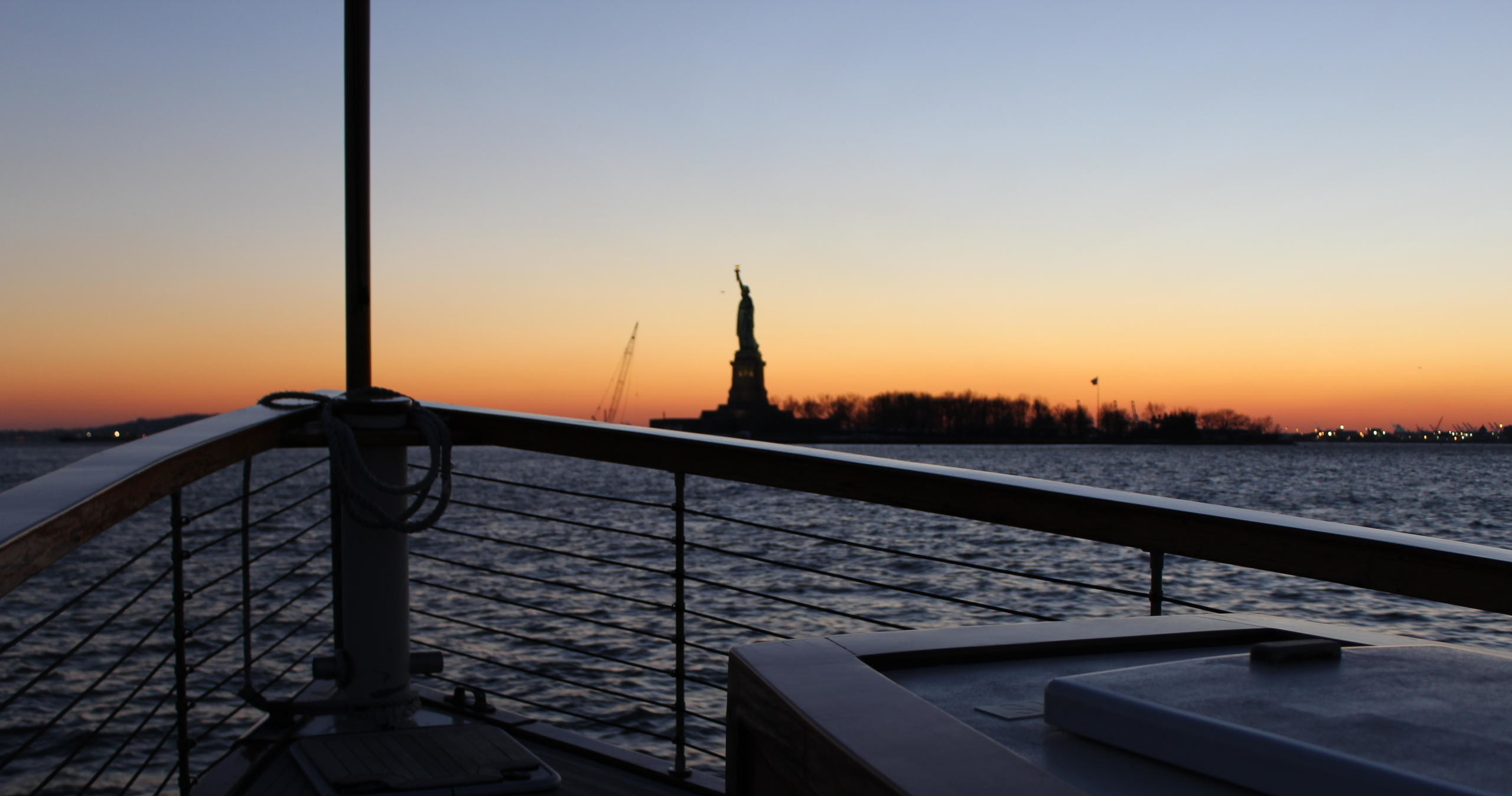 View of Statue of Liberty from a boat at sunset, railing in foreground.