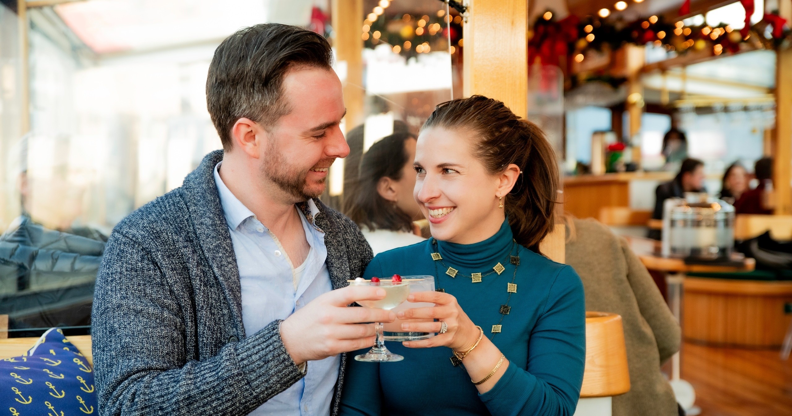 Couple smiling and toasting with drinks in a cozy, festive setting.