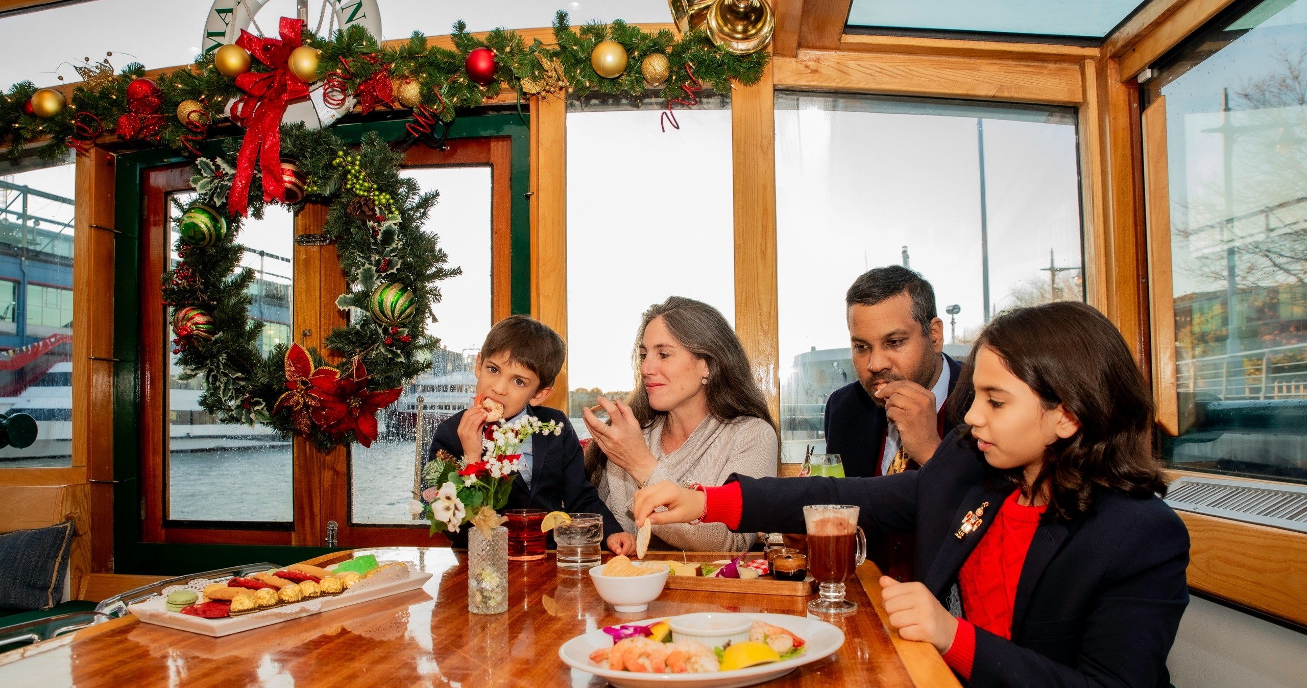 Family enjoying holiday meal on decorated boat with wreath and ornaments.