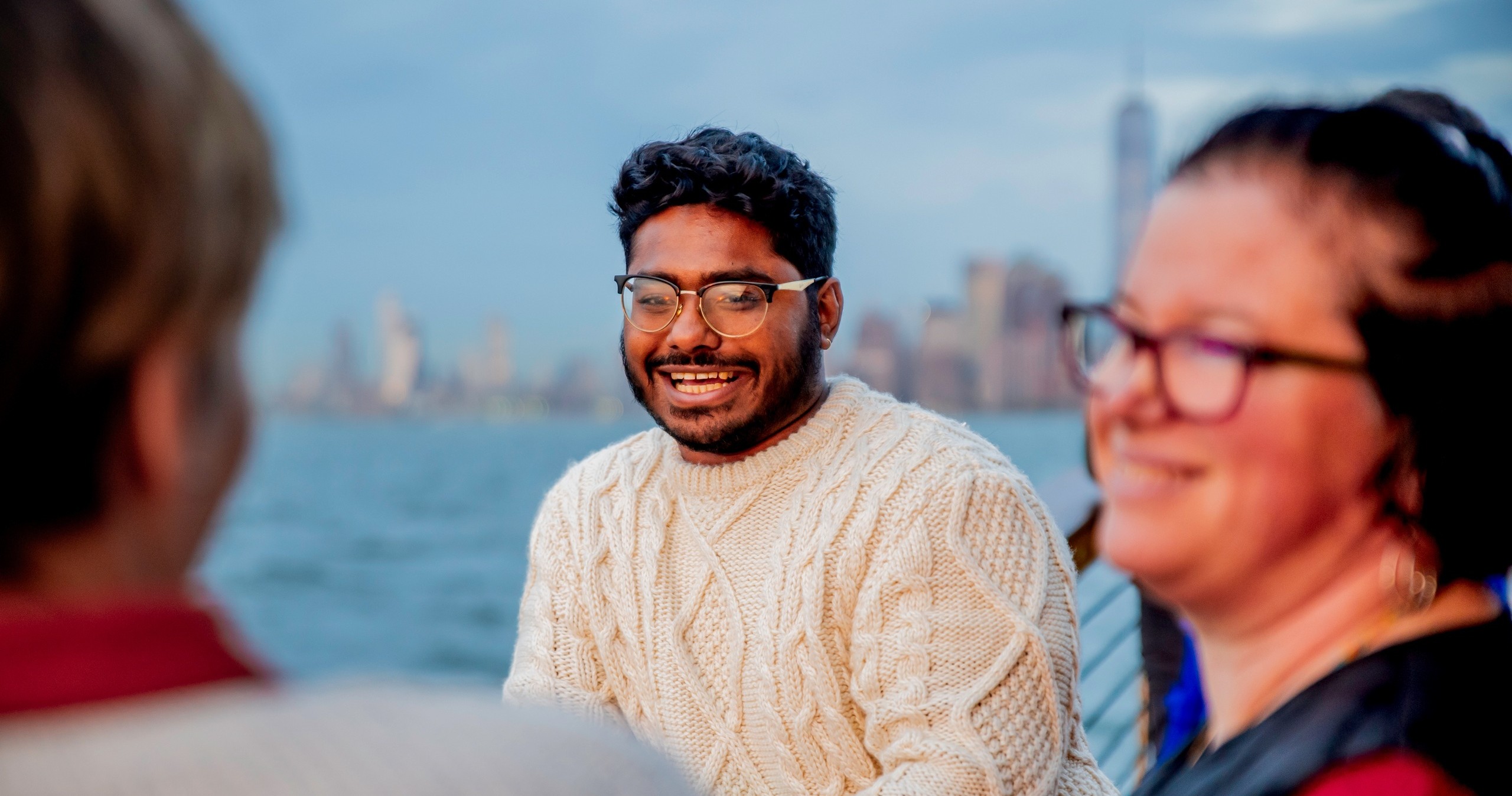 Smiling person in sweater on boat with blurred cityscape background.