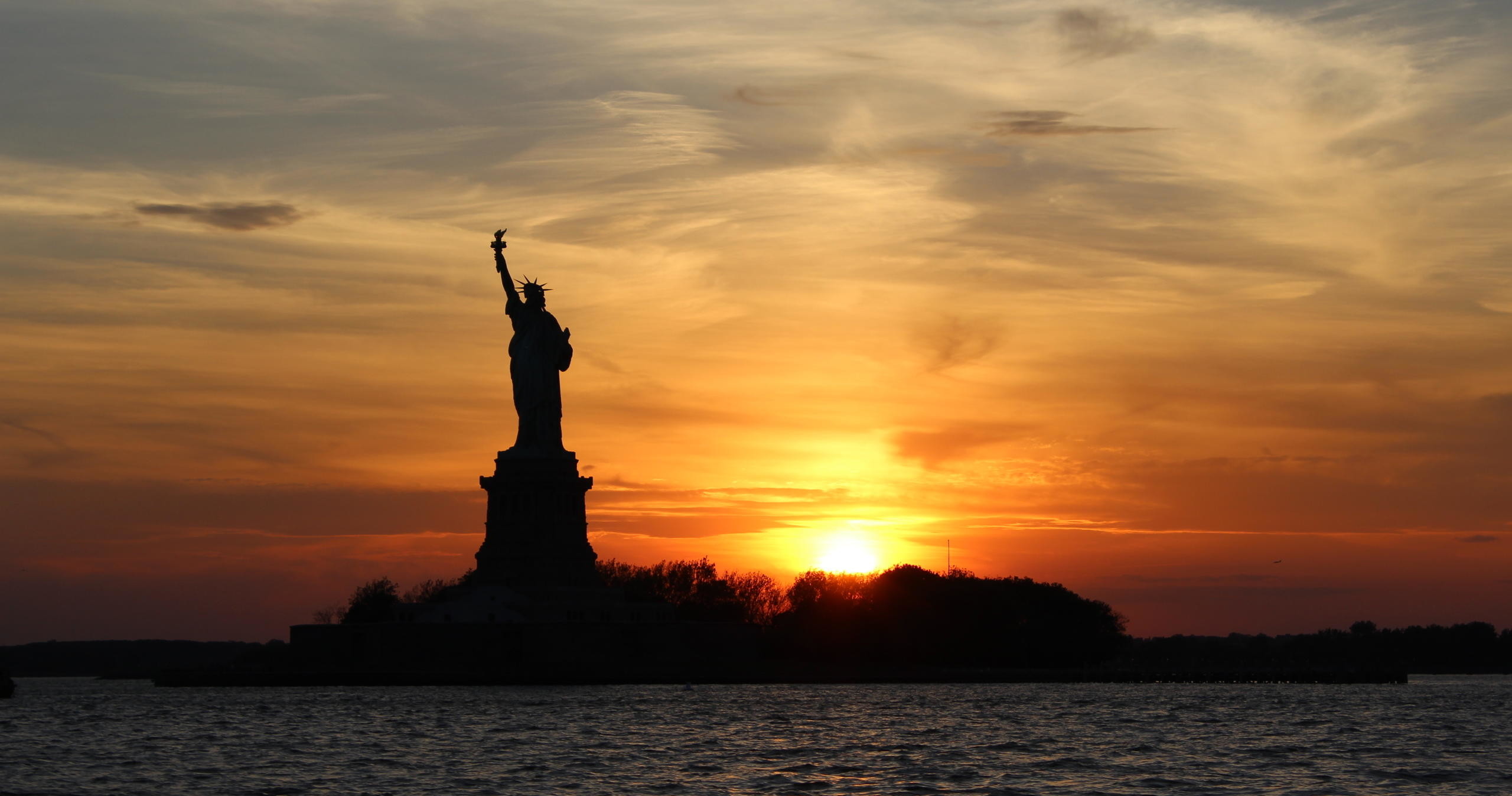 Silhouette of the Statue of Liberty at sunset over water.