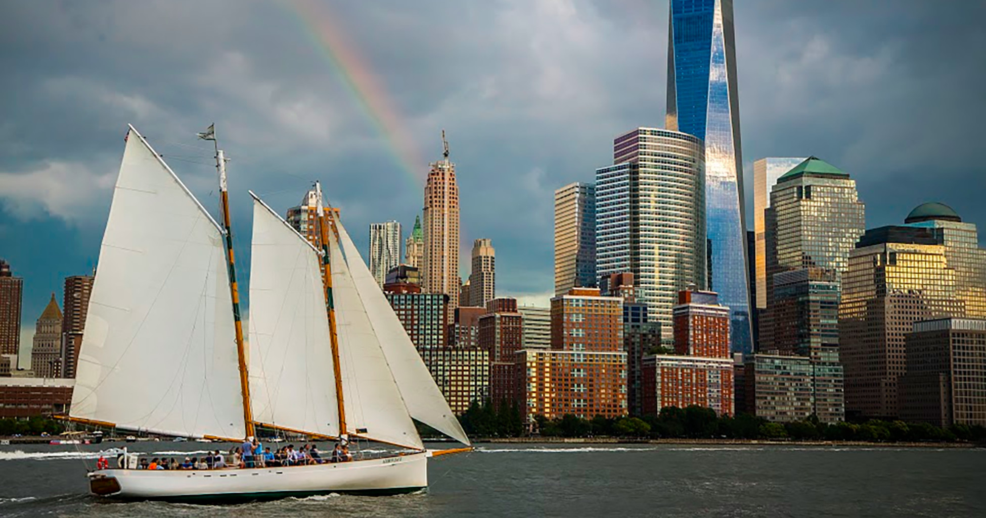 Sailboat on water with city skyline and rainbow in the background.
