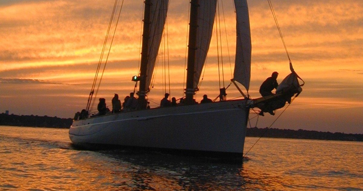 Silhouetted sailboat with people against an orange sunset over water.