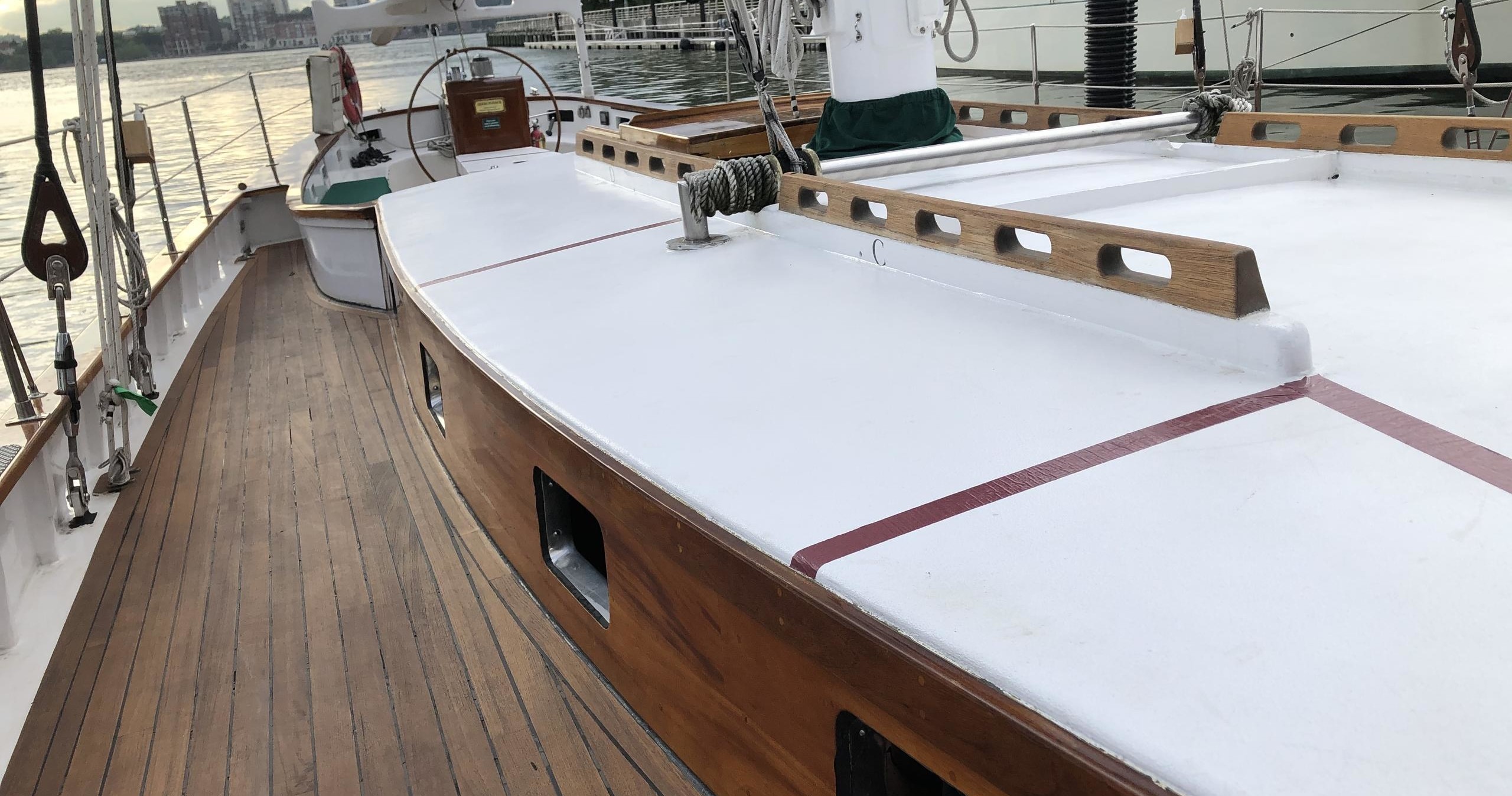 Wooden deck of a sailboat with a white cabin roof and ropes.