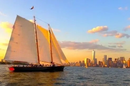 Sailboat on water at sunset with city skyline in background.