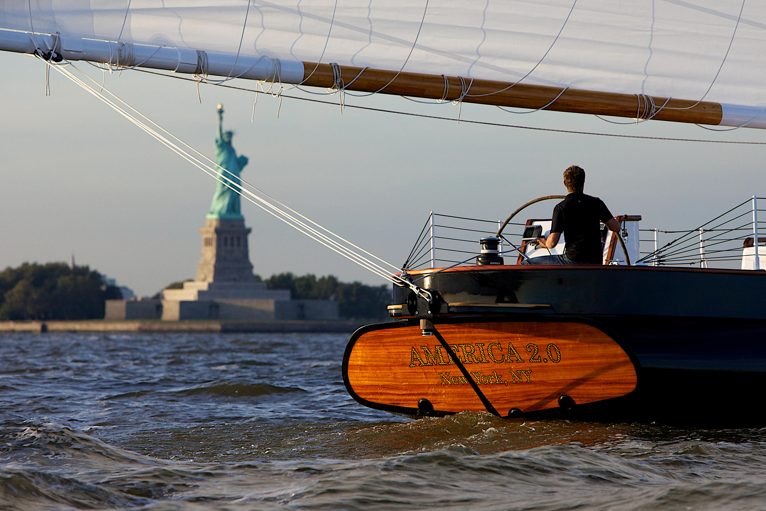 Sailboat in water near Statue of Liberty at sunset.
