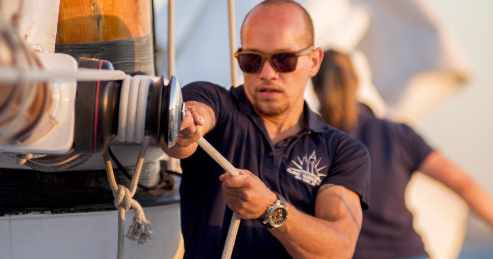 Person with sunglasses handling ropes on a boat.