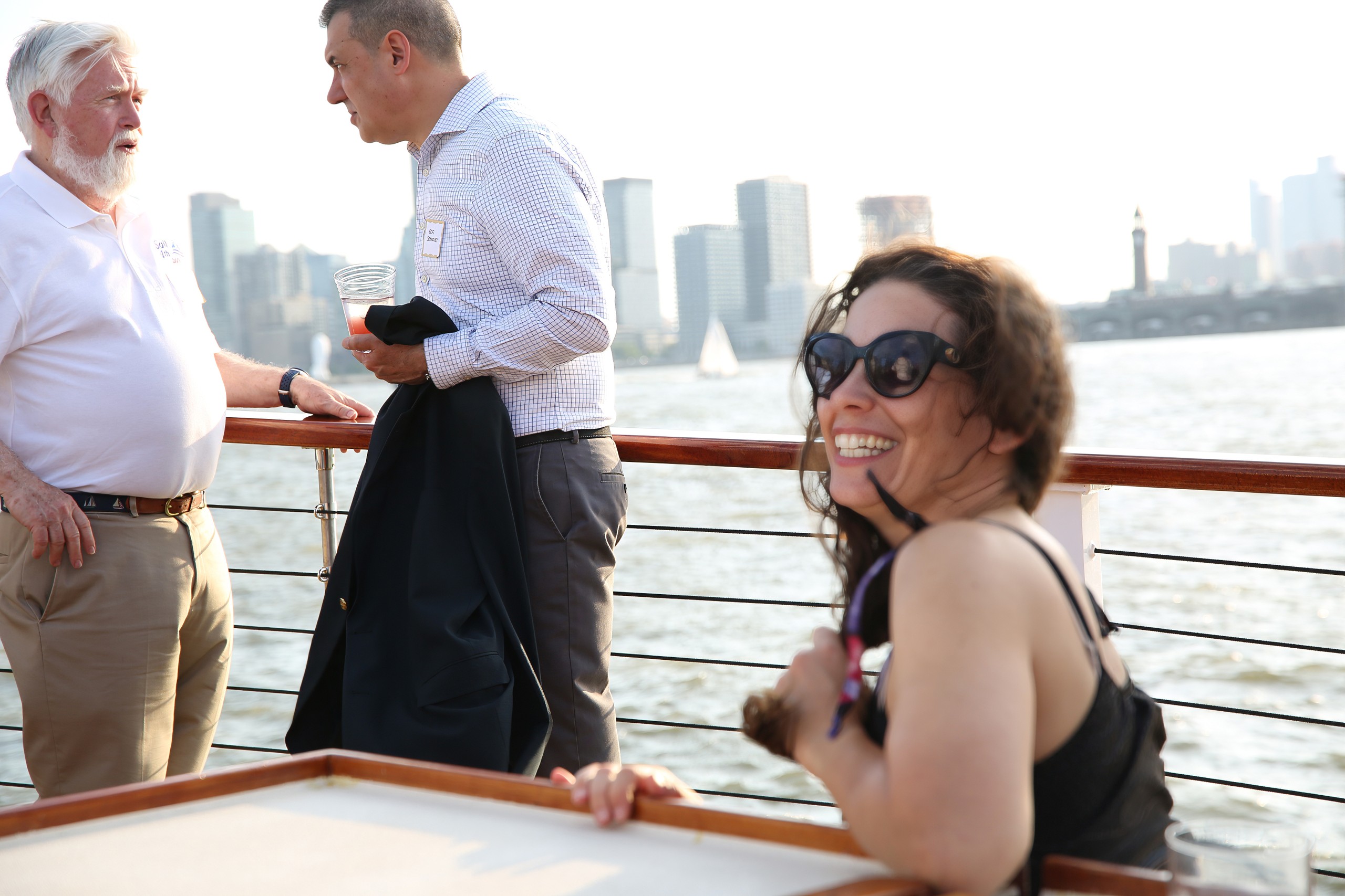 Three people on a boat deck with a city skyline in the background.