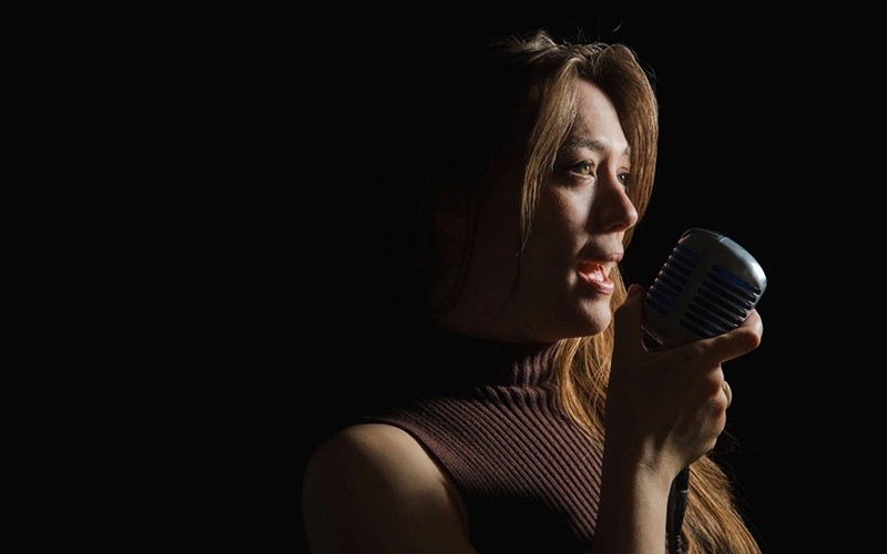 Woman singing into vintage microphone on a dark background.