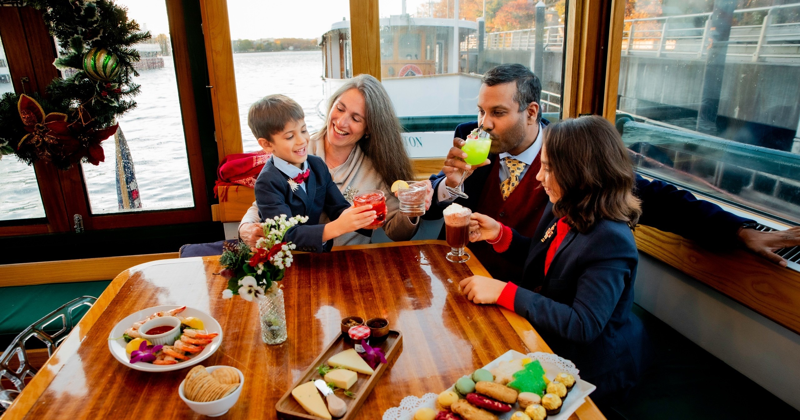 Family toasting inside boat with appetizers on table.
