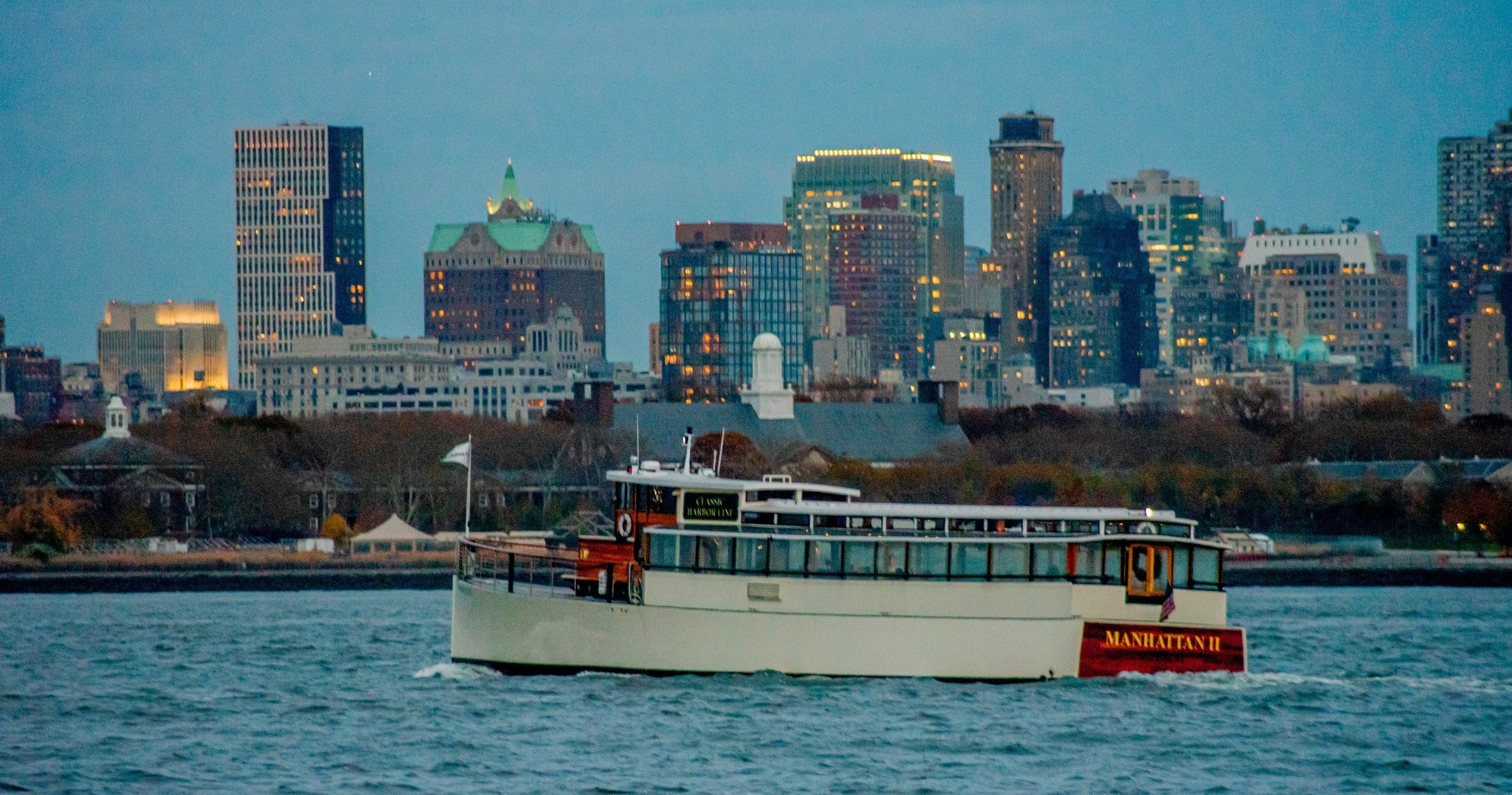 Boat on water with city skyline at dusk in background.