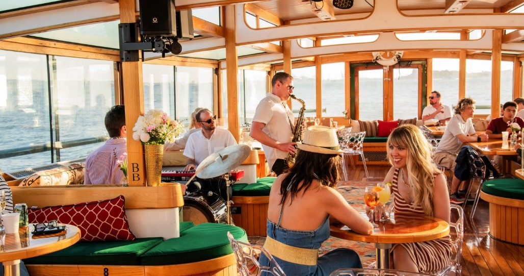 People enjoying a boat ride with live saxophone music and sunset view.