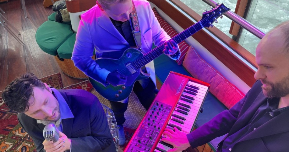 Three musicians on a boat, with microphone, guitar, and keyboard.