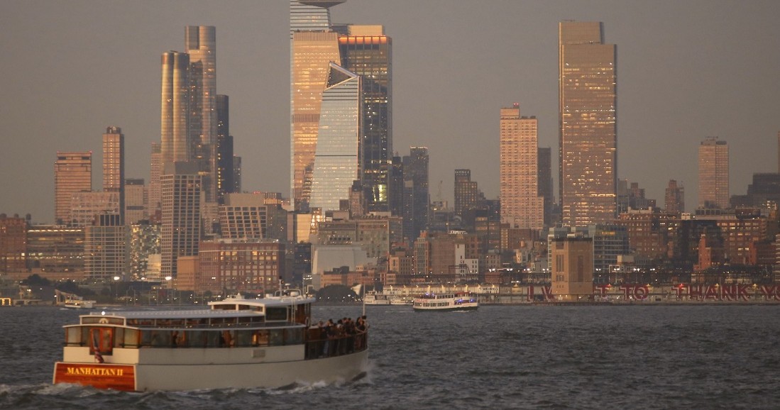 Boat on water with tall city skyline visible at dusk.