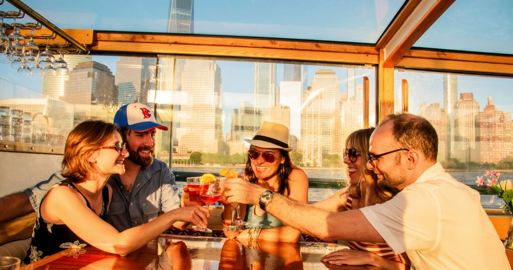 Five people toasting drinks at rooftop bar with cityscape view.