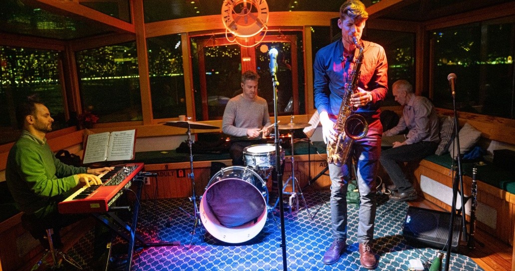 Jazz band playing instruments on a cozy boat with city lights outside.
