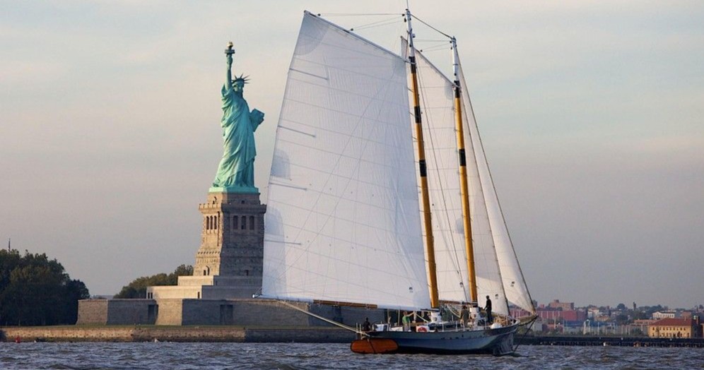 Sailboat passing by the Statue of Liberty on a cloudy day.