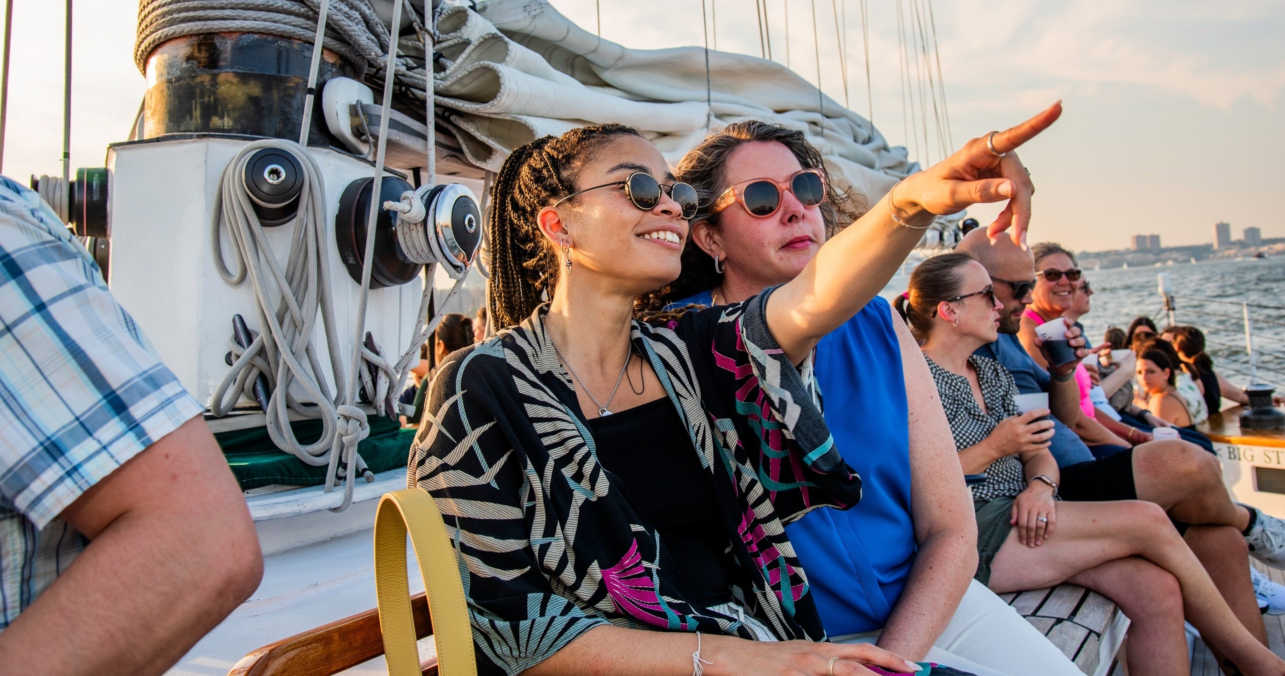 Two women smiling and pointing on a boat, with other people in the background.