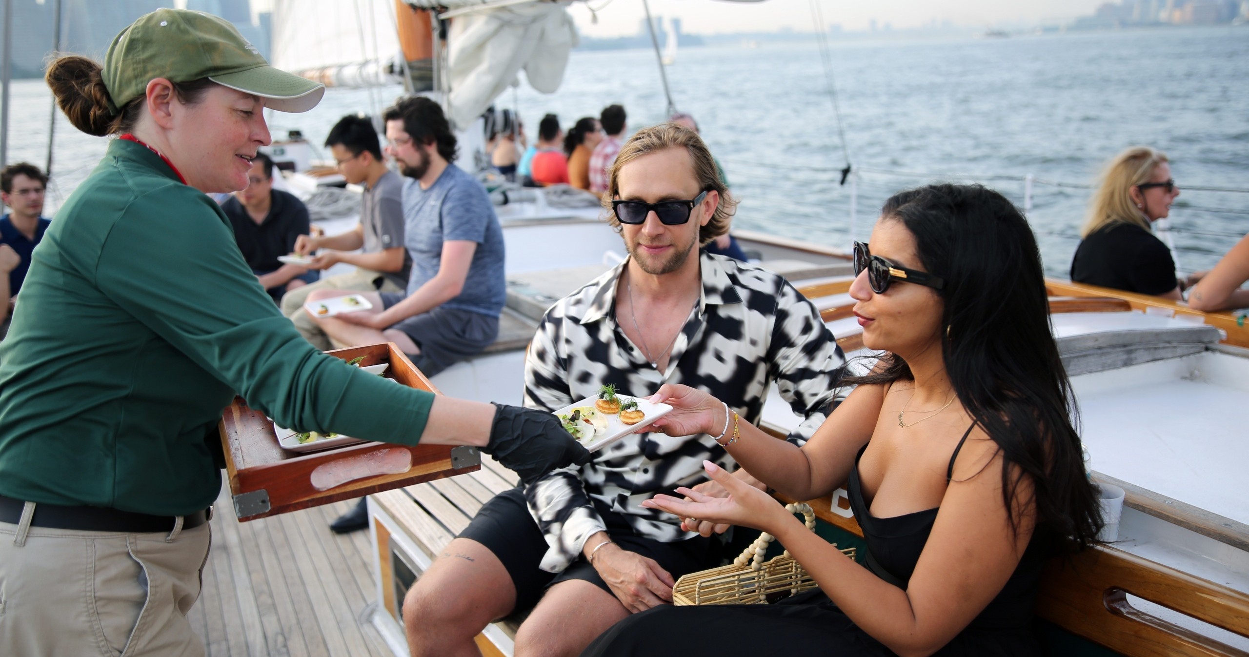 People enjoying food on a boat deck with skyline in the background.