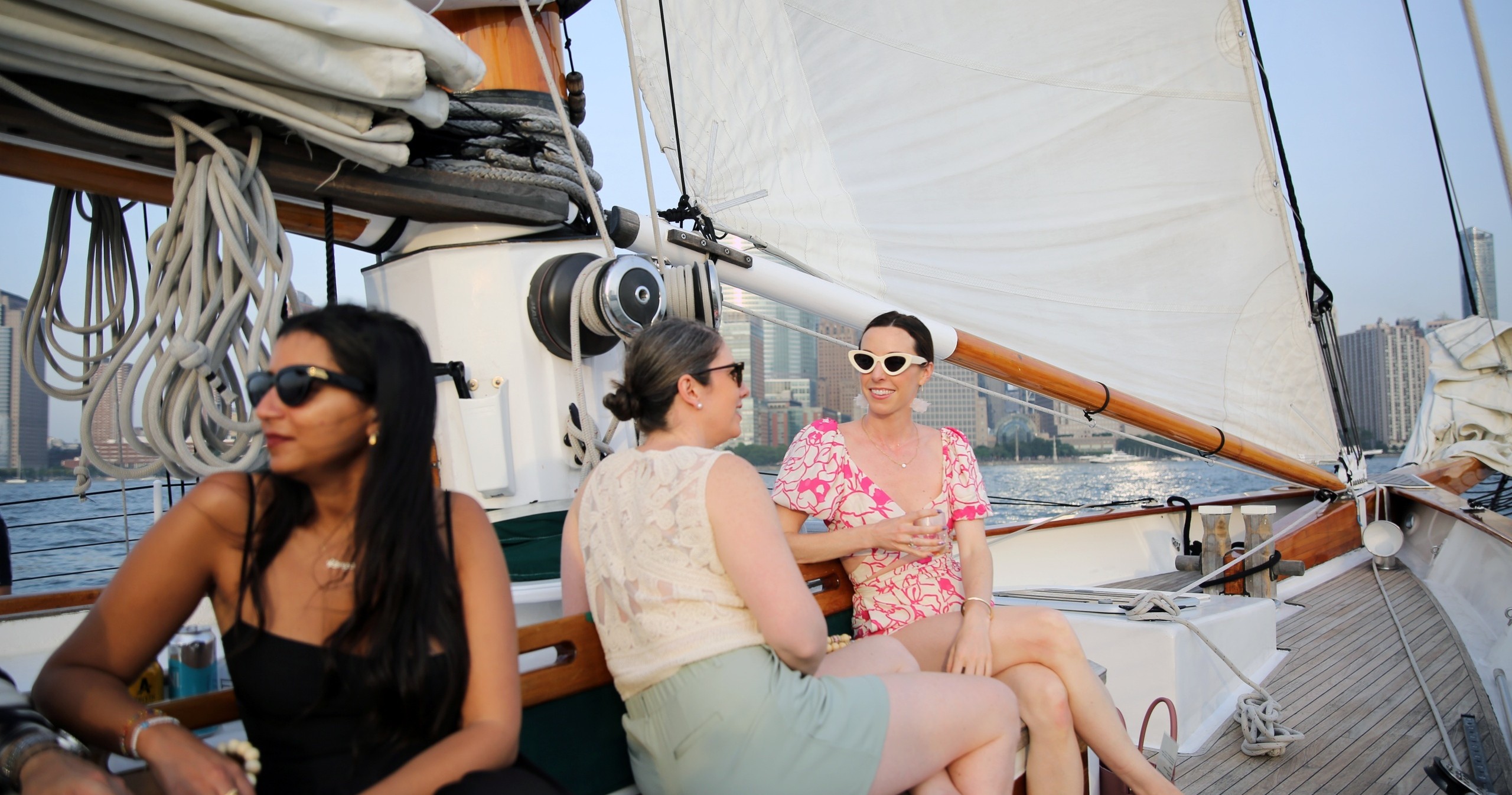 Three women chatting on a sailboat, with city skyline in the background.