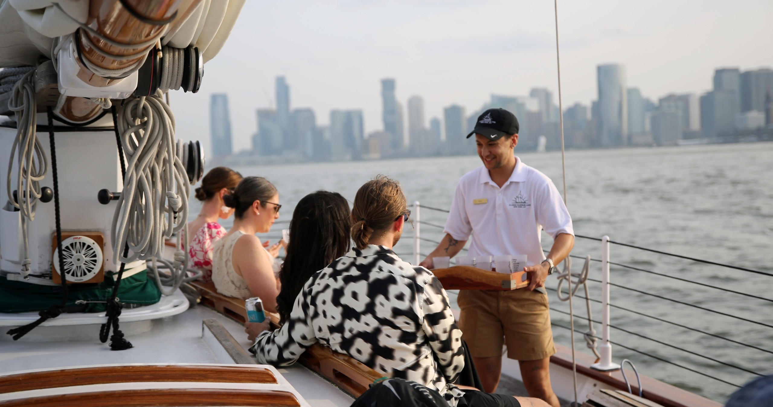 Group of people on a sailboat with city skyline in the background.