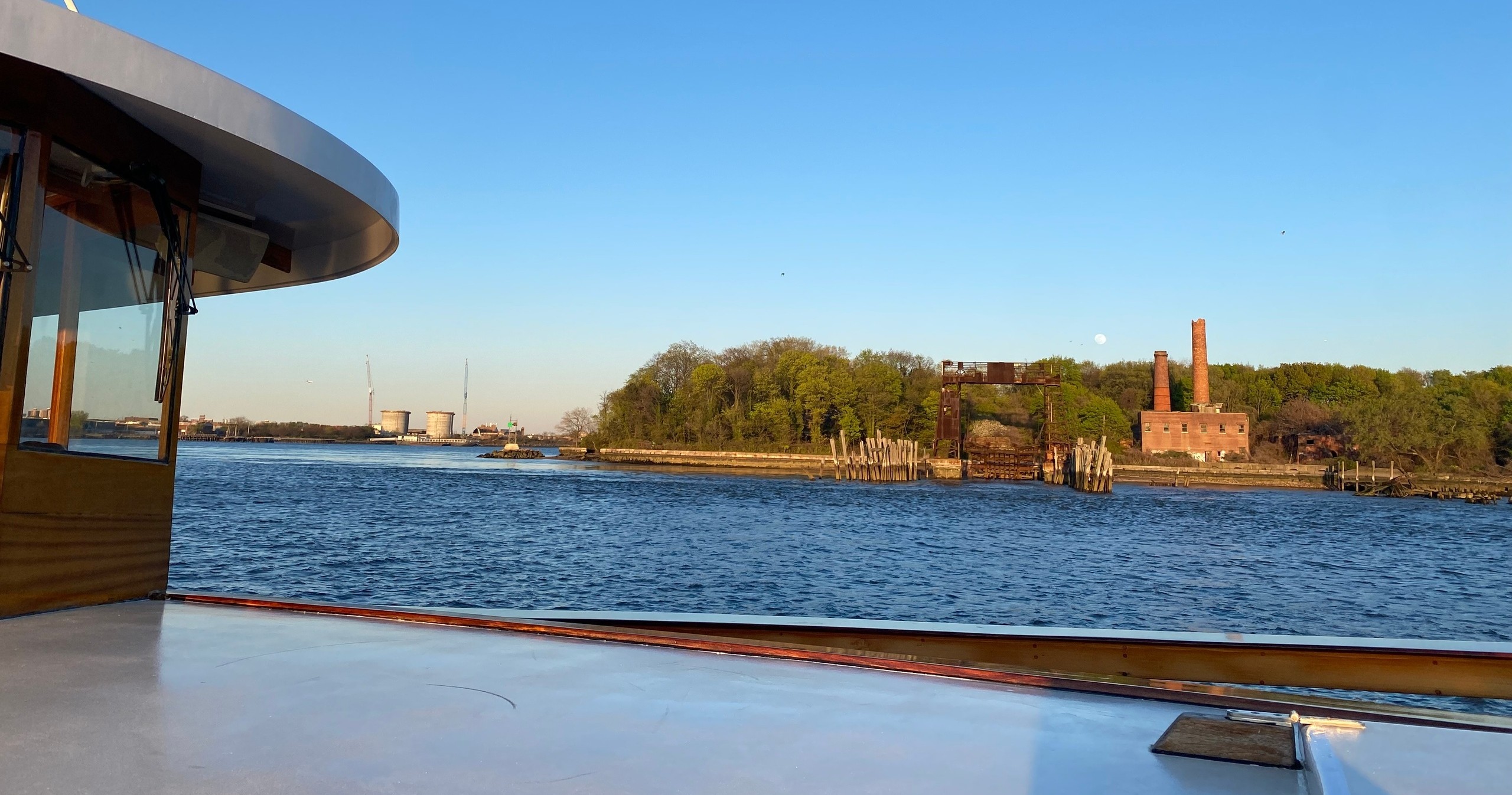 Boat deck view of river, green trees, and brick building.