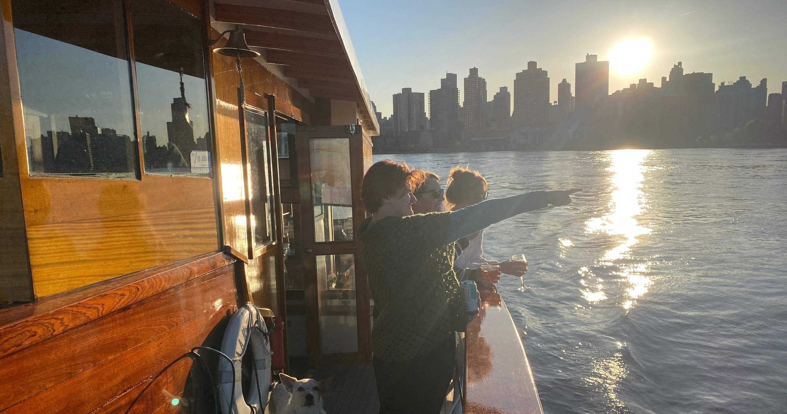 People on a boat enjoy a sunset view of a city skyline across the water.
