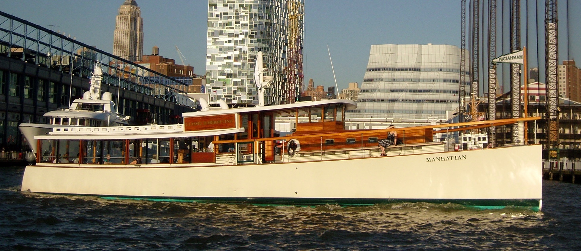 A vintage-style boat named Manhattan on a city waterfront.