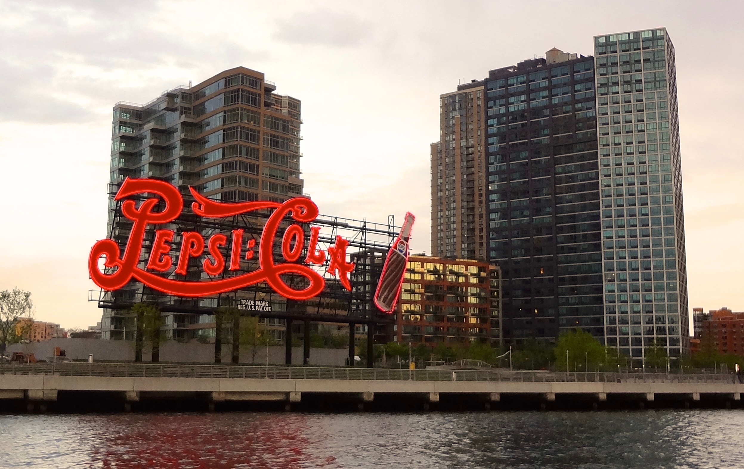Pepsi-Cola sign with skyscrapers behind in dusk light by the waterfront.