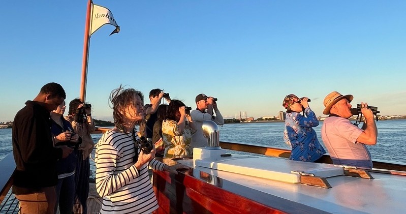 People on a boat observing with binoculars by a body of water.