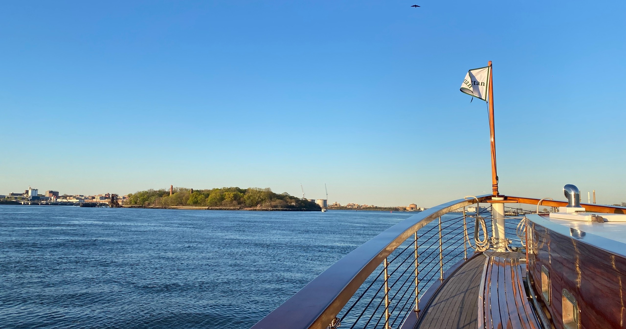 Boat deck view of island and clear blue sky in daytime.