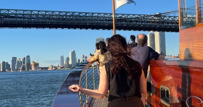 People on a boat approaching a bridge with a city skyline in the background.