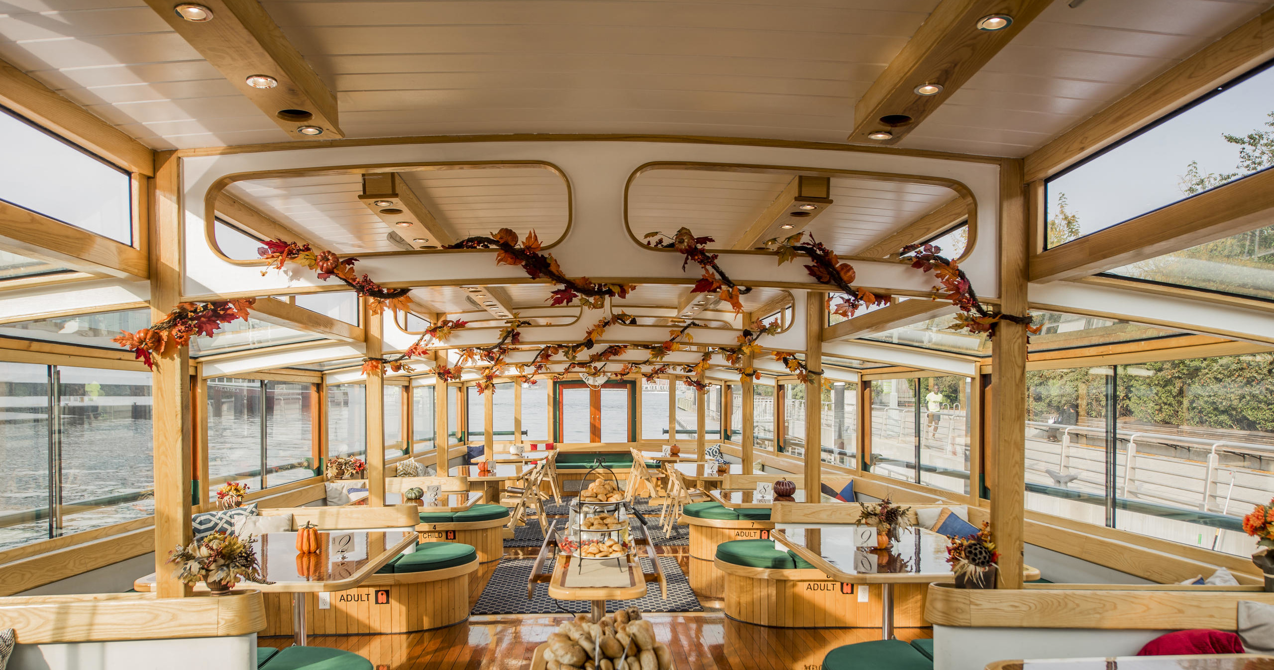 Cozy boat interior with wooden tables, green cushions, and autumn decor.