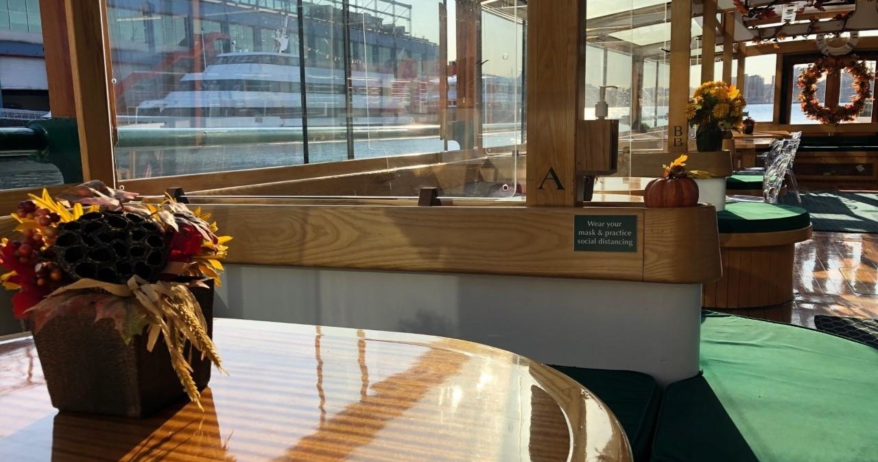 Sunlit boat interior with autumn decorations and a view of a docked ship outside.