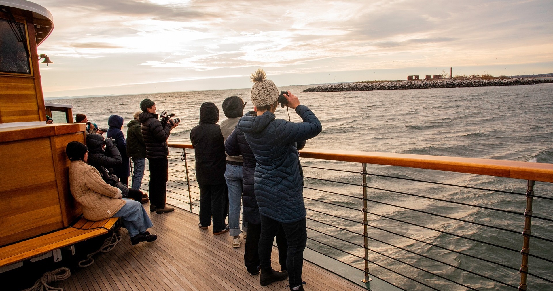 People on a boat deck taking photos of the ocean and distant rocks.