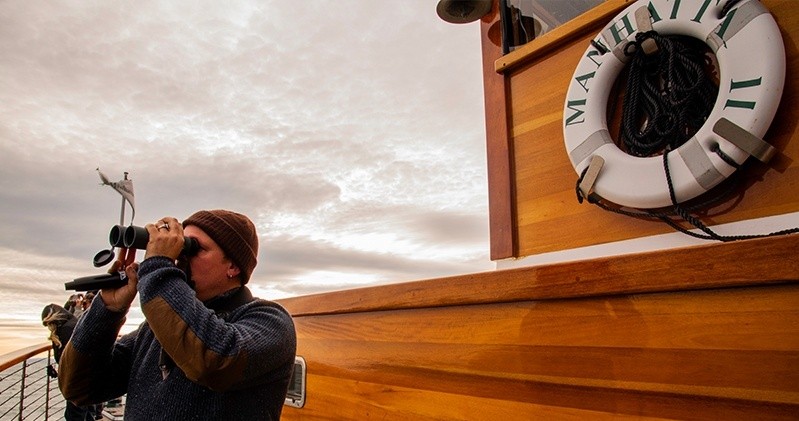 Person on boat with binoculars, life preserver labeled 'MANHATTAN II' visible.