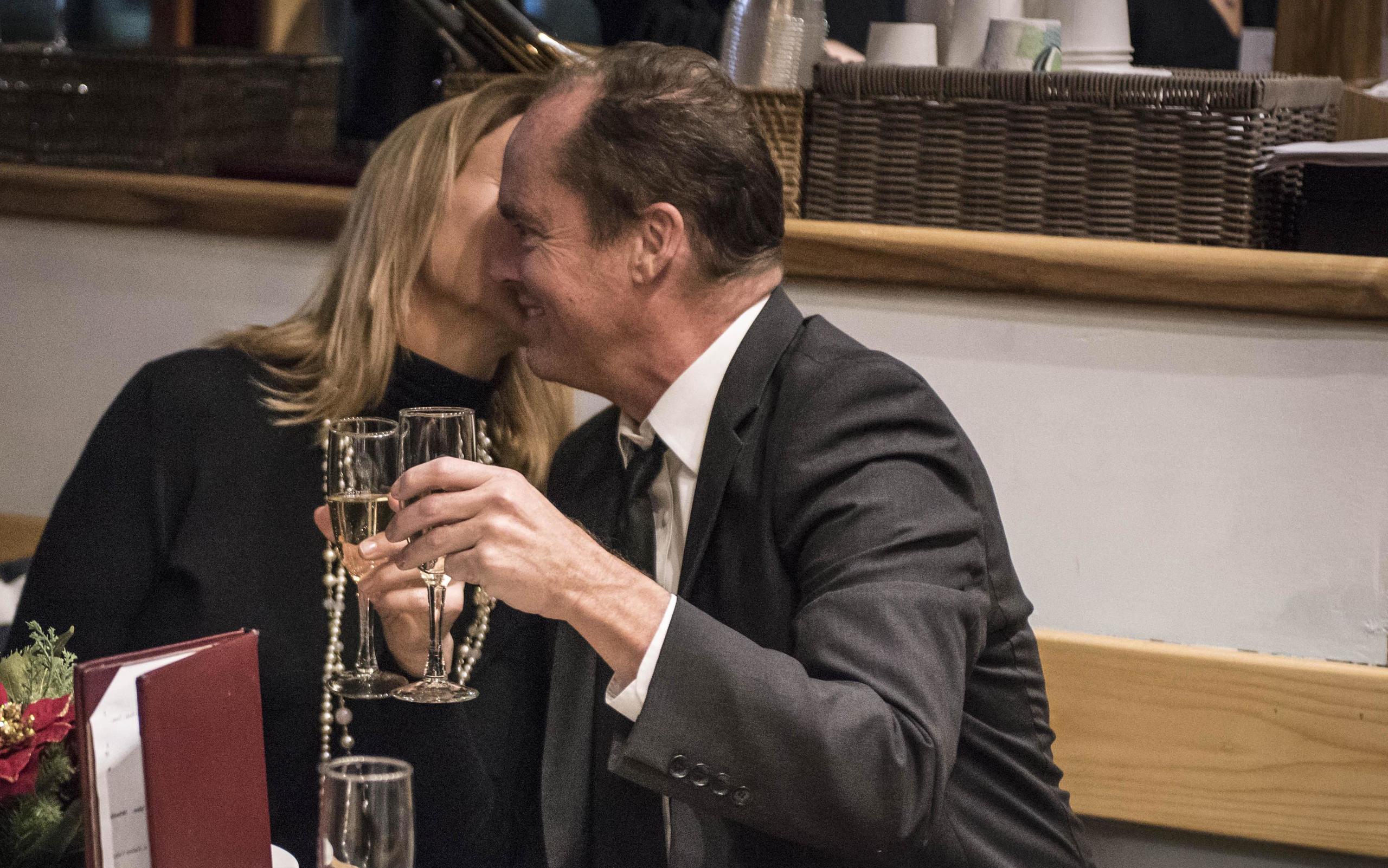 Two people in formal attire smiling and clinking glasses at a restaurant.