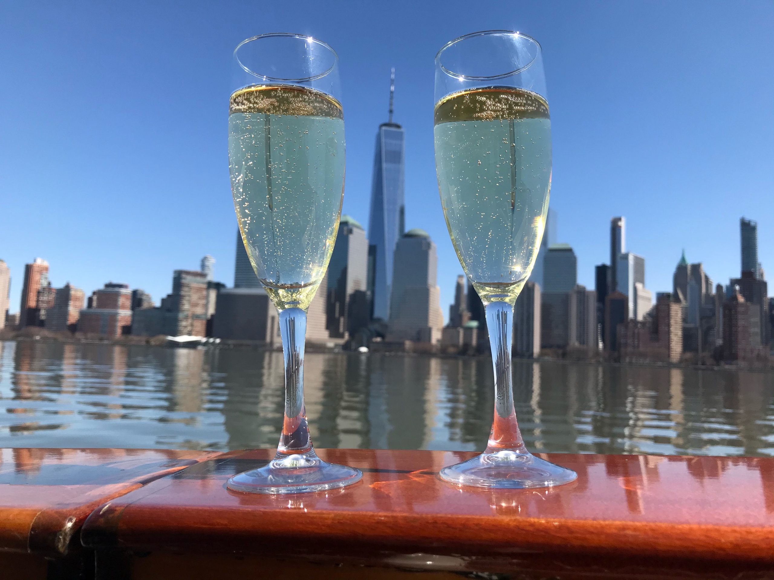 Two champagne glasses with city skyline and water reflections in the background.