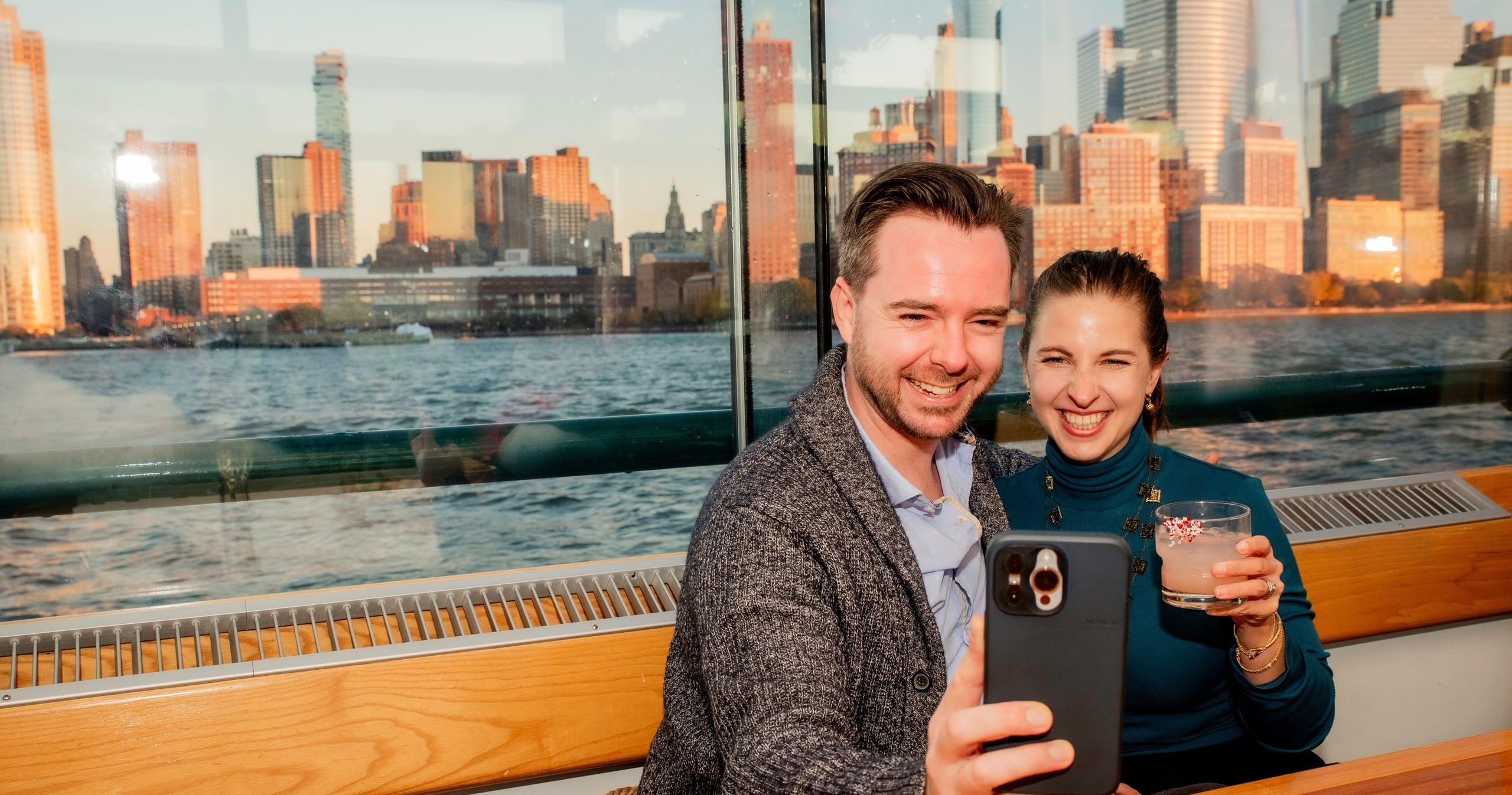 Couple taking a selfie on a boat with city skyline in background.