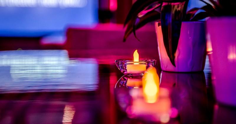 Small candles and plant on reflective surface with purple lighting.