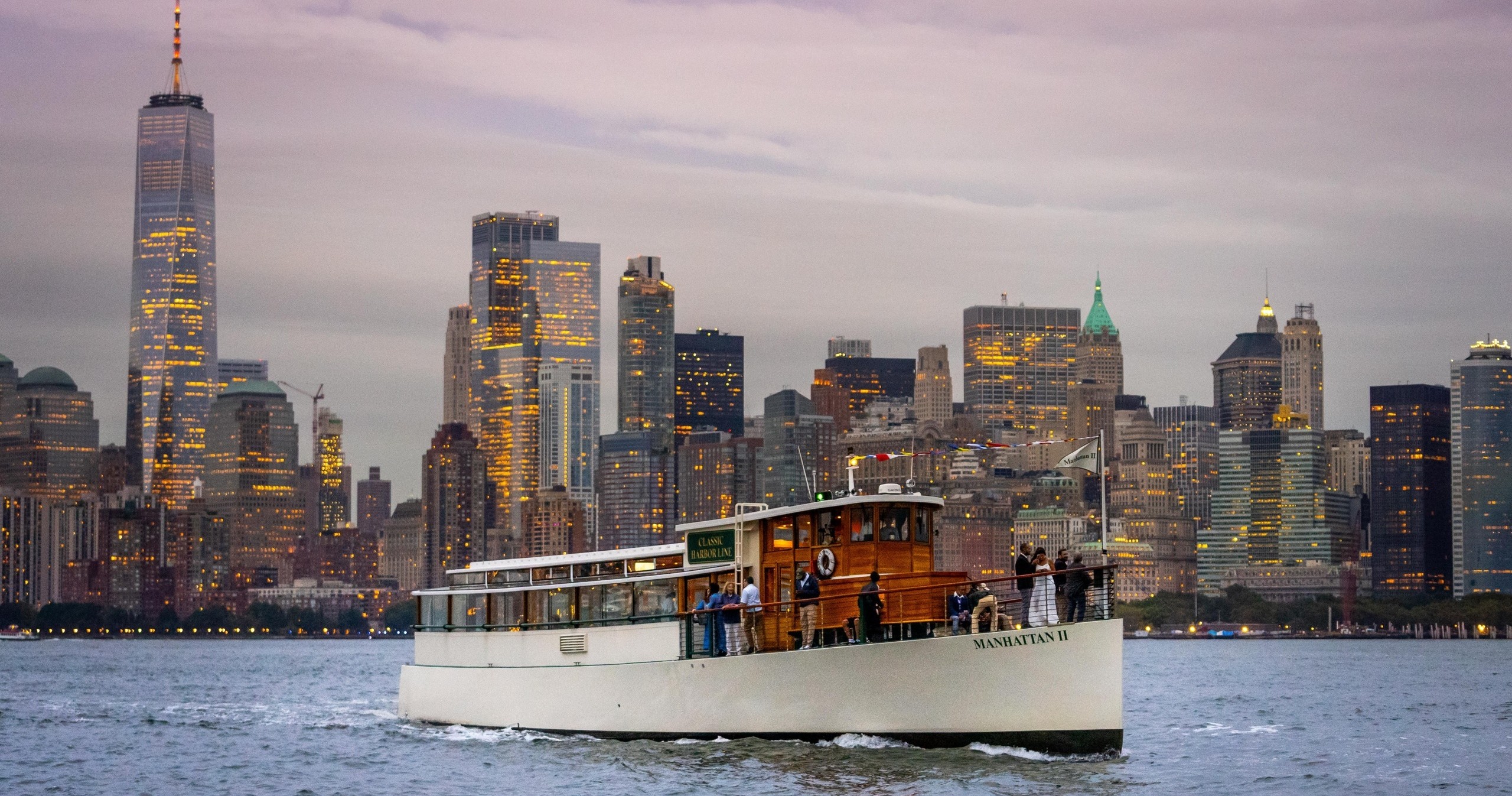 Boat sailing on river with city skyline in background at dusk.