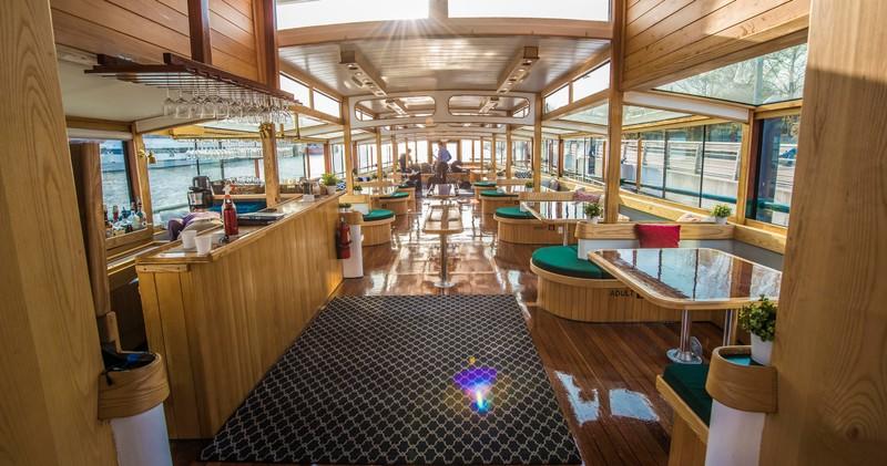 Wooden interior of a boat with tables, sunlight through windows.