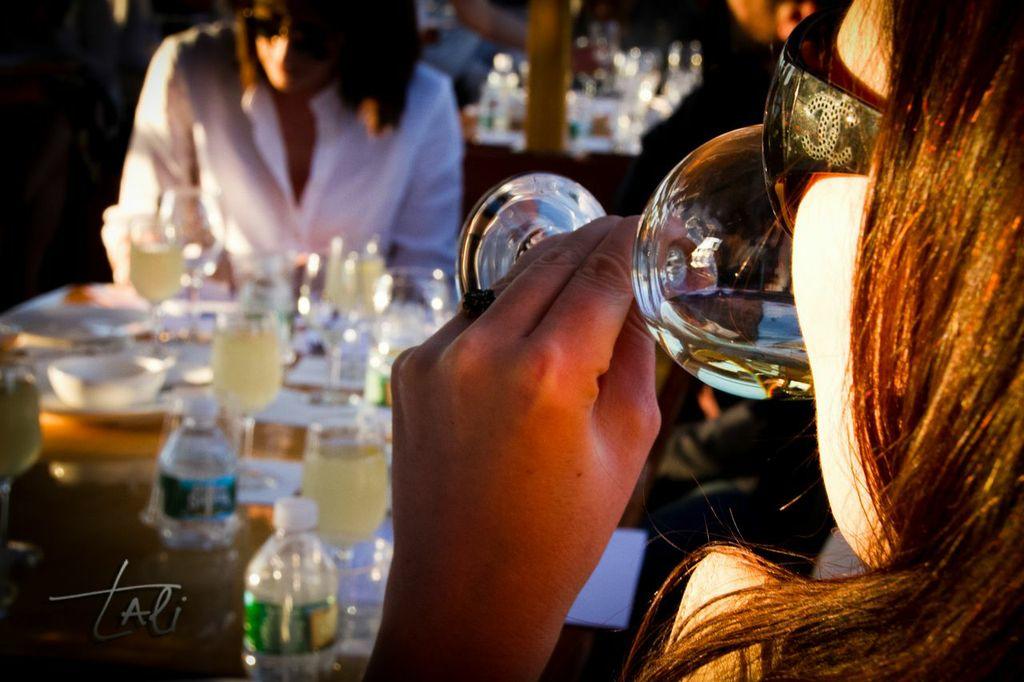 Person sipping wine at a table set with drinks and glasses.