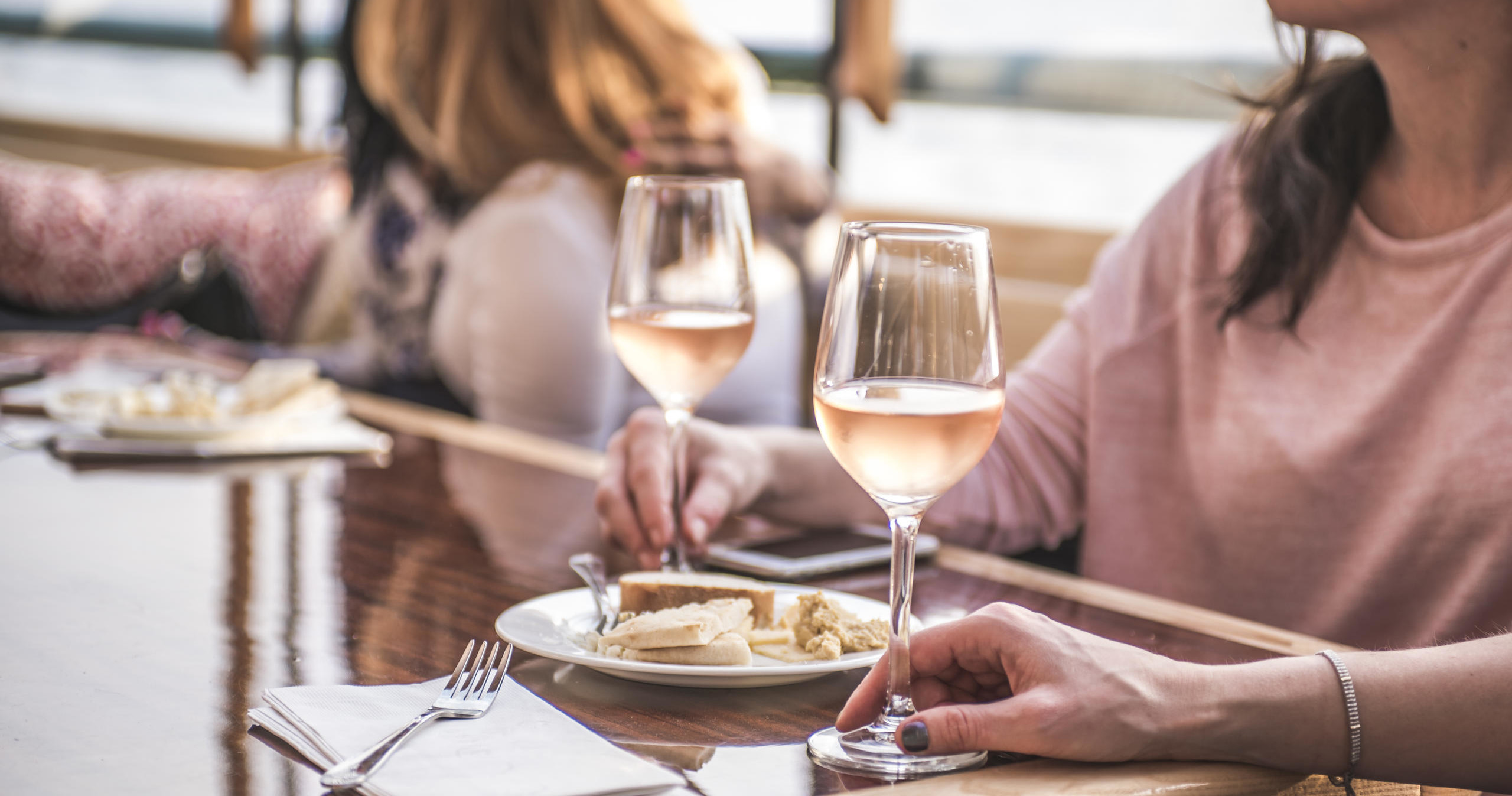 Two women at a table with wine glasses and plates of food.